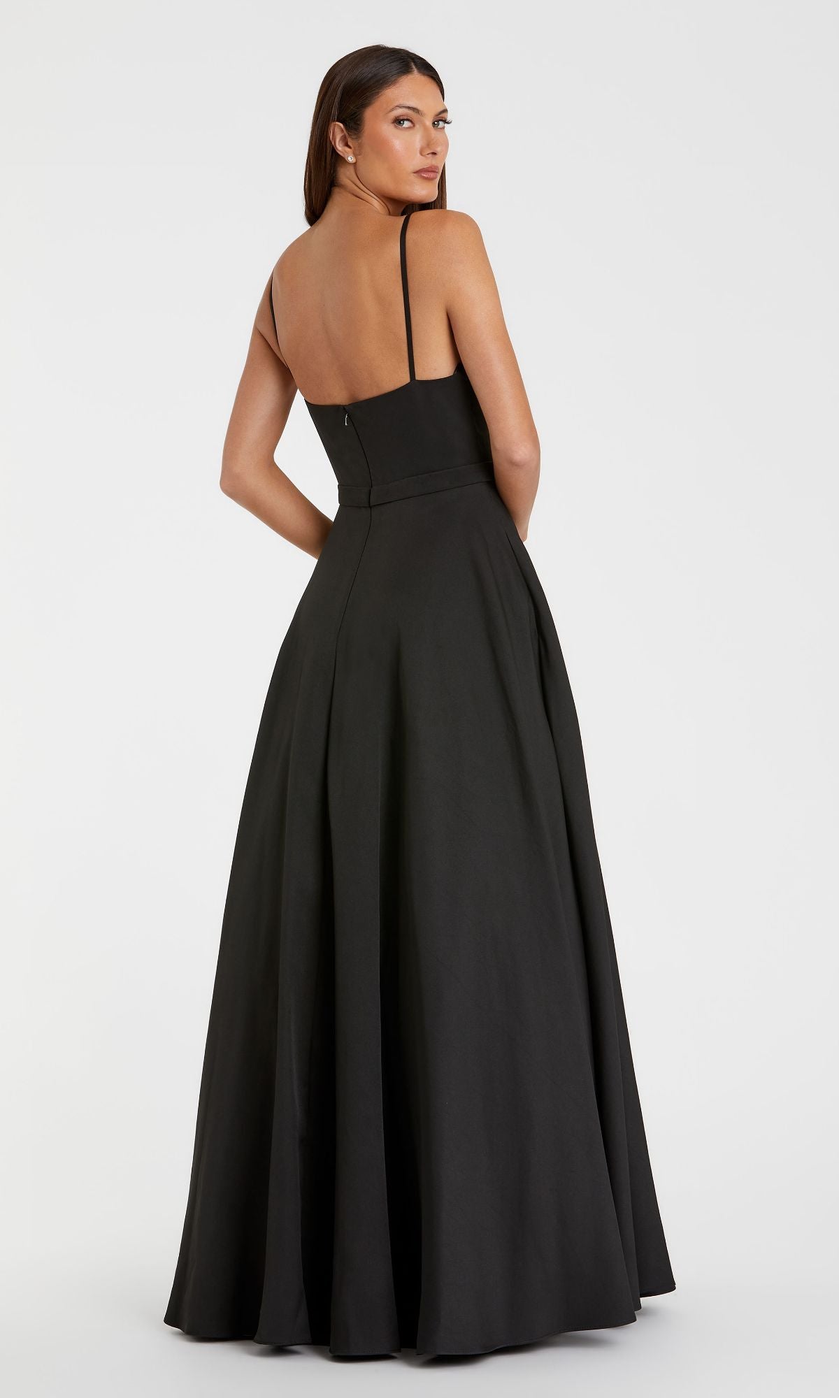 A woman models the Mac Duggal 48855 Classic Long A-Line Formal Dress, featuring thin shoulder straps, an open back, and a flared black skirt, standing against a plain light background.